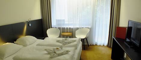 Habitación de hotel con cama, dos sillas, una mesita, televisor y ventana con cortinas.