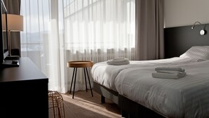 A hotel room with a bed, a desk, a lamp, and a view of the outdoors through sheer curtains. - Hotel Am Fang (Bad Laasphe)