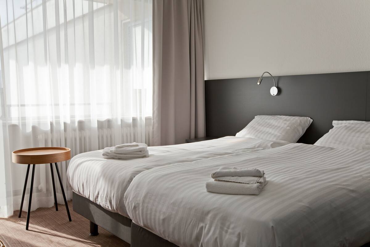 Una habitación de hotel moderna con una cama grande, una mesita de madera redonda y un aplique de pared.