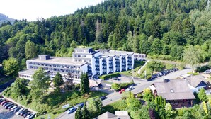 A multi-story hotel with a modern design, surrounded by lush greenery and a parking area. - Hotel Am Fang (Bad Laasphe)