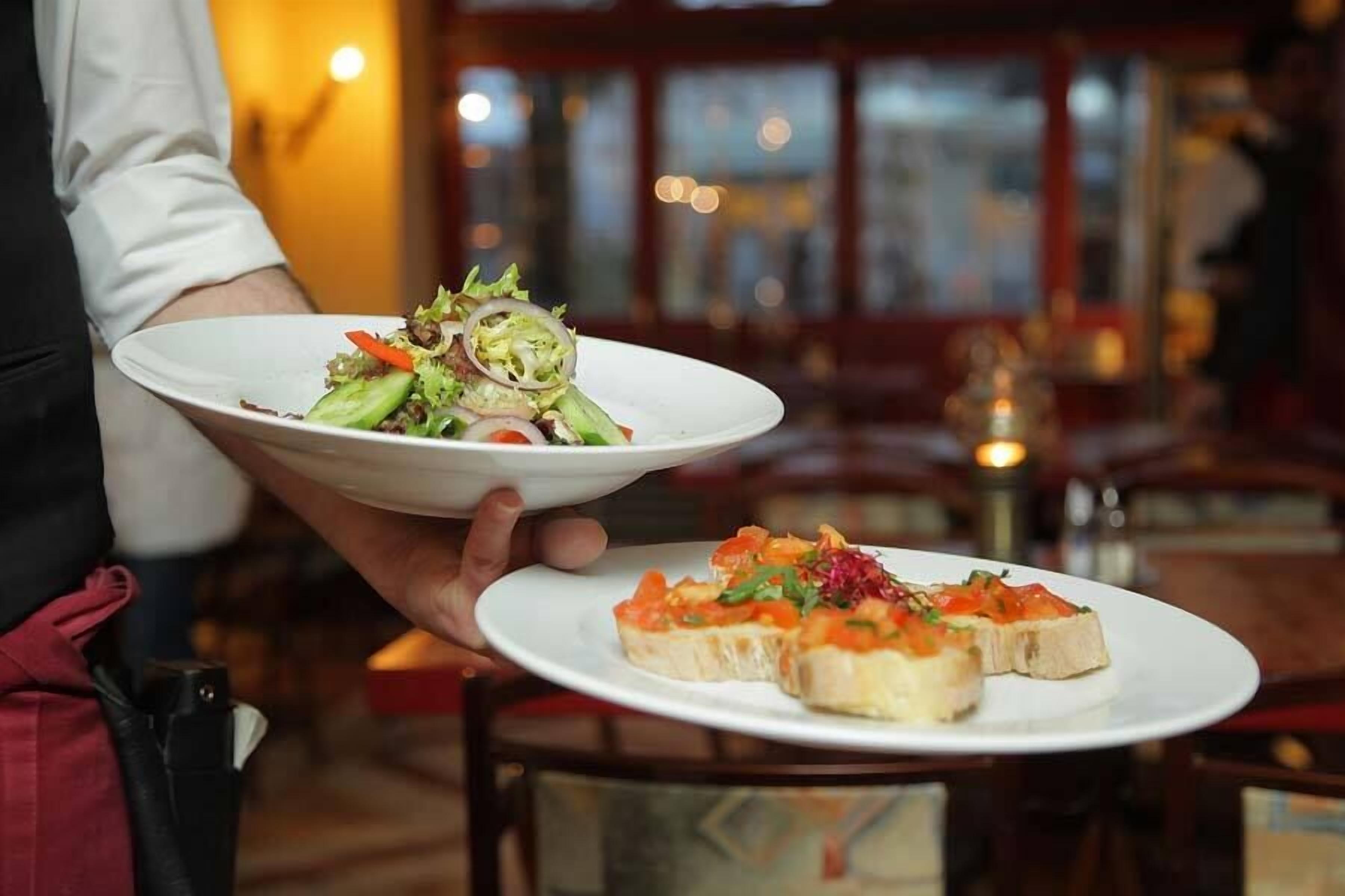 A person holding two plates, one with a salad and the other with bruschetta.