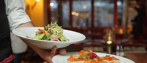 Una persona sosteniendo dos platos, uno con una ensalada y otro con bruschetta.