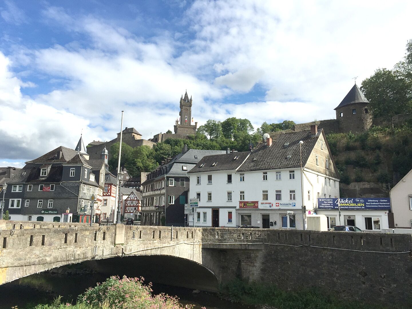 Eine historische Stadt mit einer Brücke, Gebäuden und einer Burg im Hintergrund.
