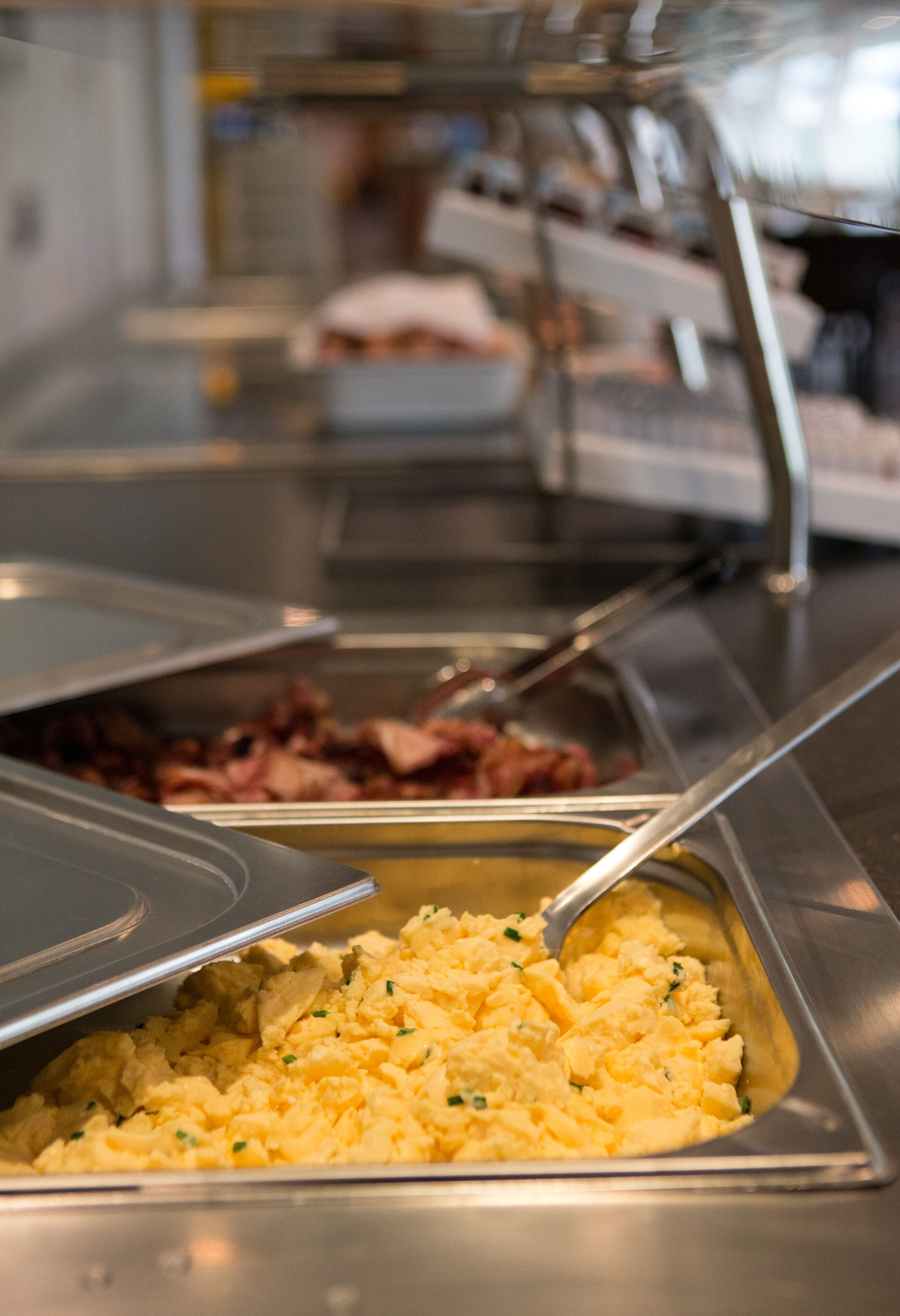 Un buffet proposant une variété de plats, notamment des œufs brouillés, du bacon et d’autres mets.