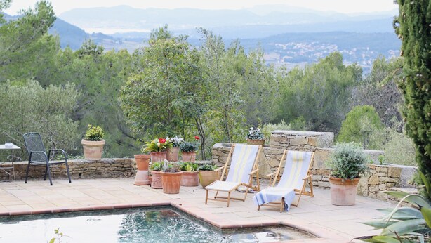 A pool area with two lounge chairs, potted plants, and a stone wall.