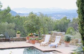 Un área de piscina con dos sillones de descanso, plantas en macetas y una pared de piedra.