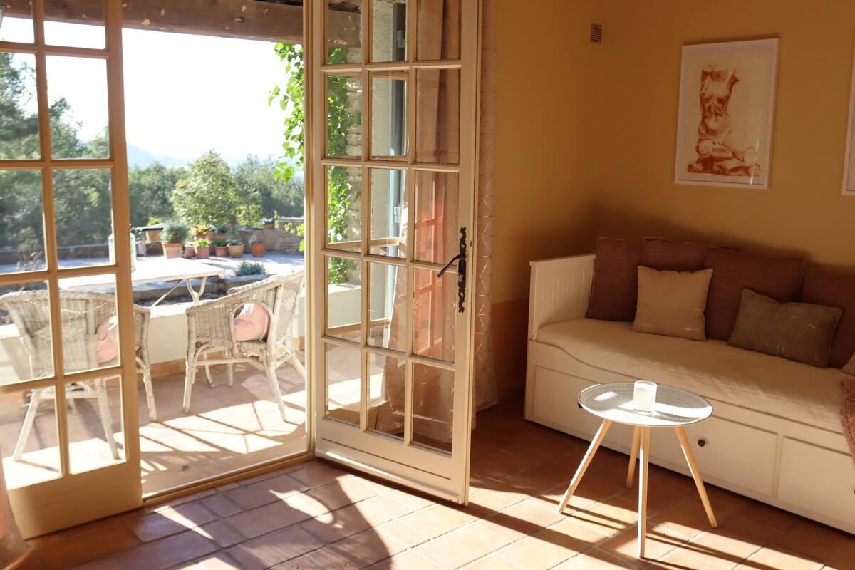 Una sala de estar acogedora con un sofá, una mesa de vidrio y vistas a un patio exterior con mobiliario de mimbre.