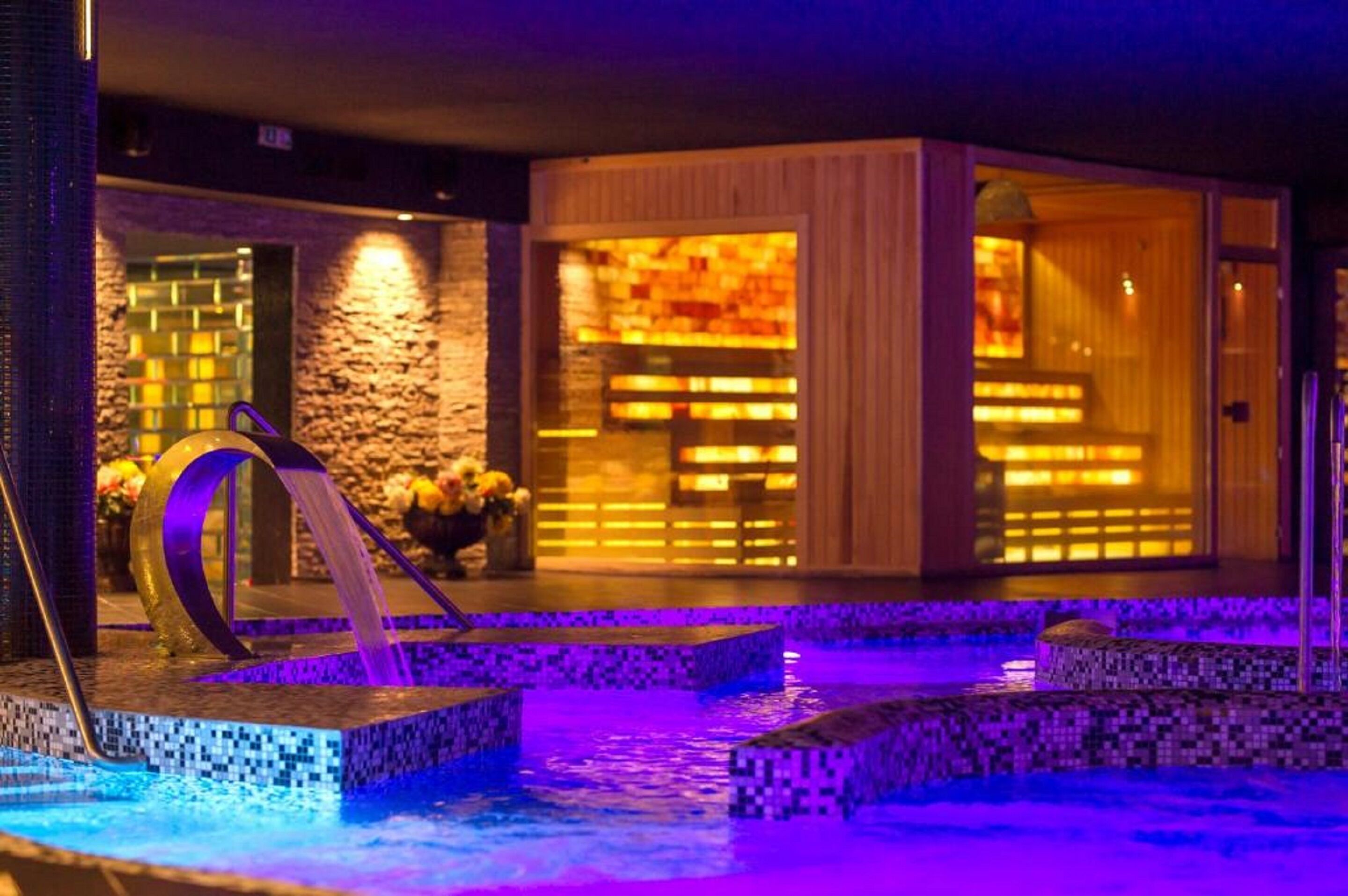 Un espacio de spa con piscina climatizada, sauna de madera y pared de piedra.