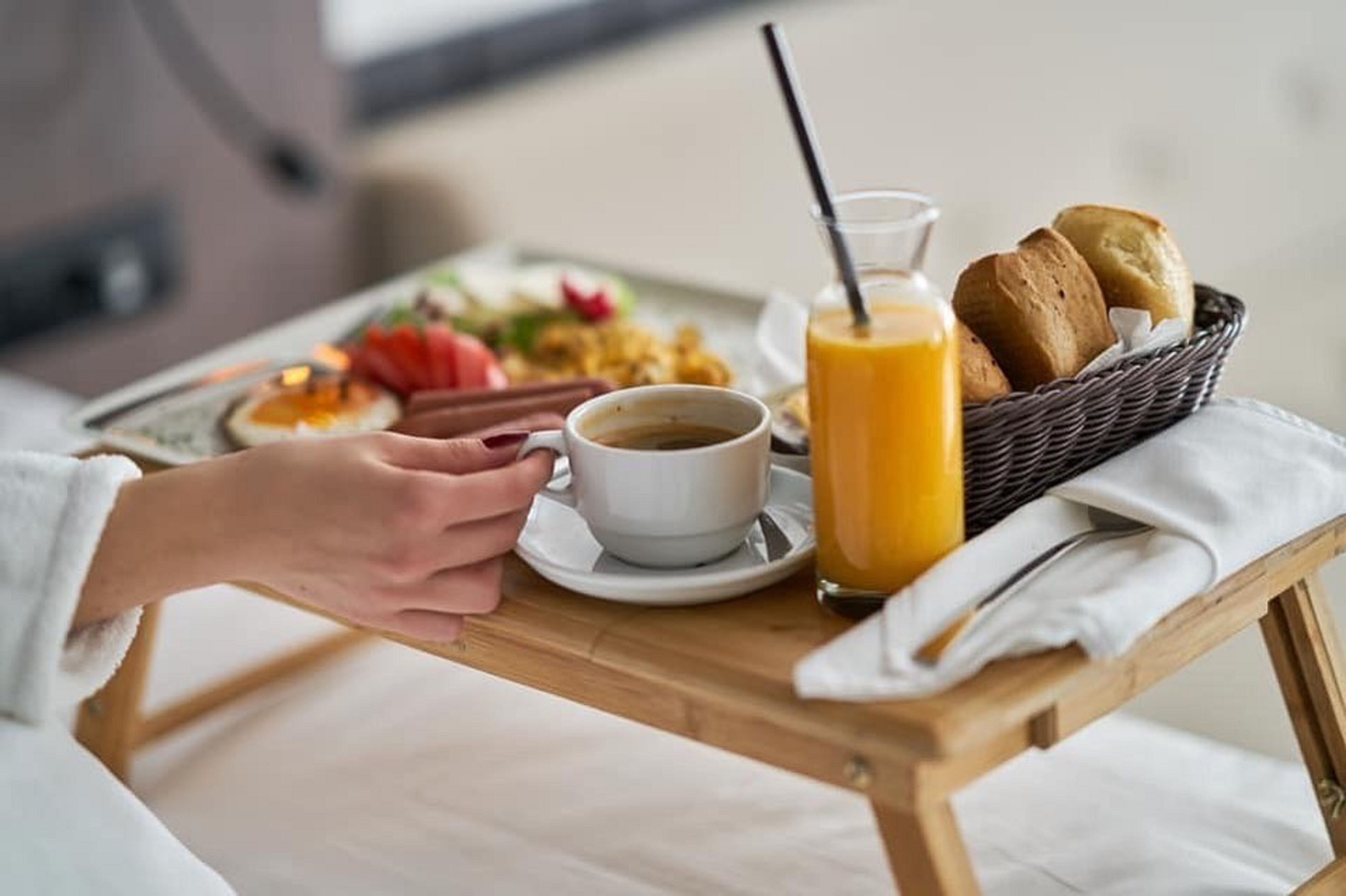 Un plateau de petit-déjeuner avec une tasse de café, un verre de jus d’orange et du pain, posé sur une table en bois.
