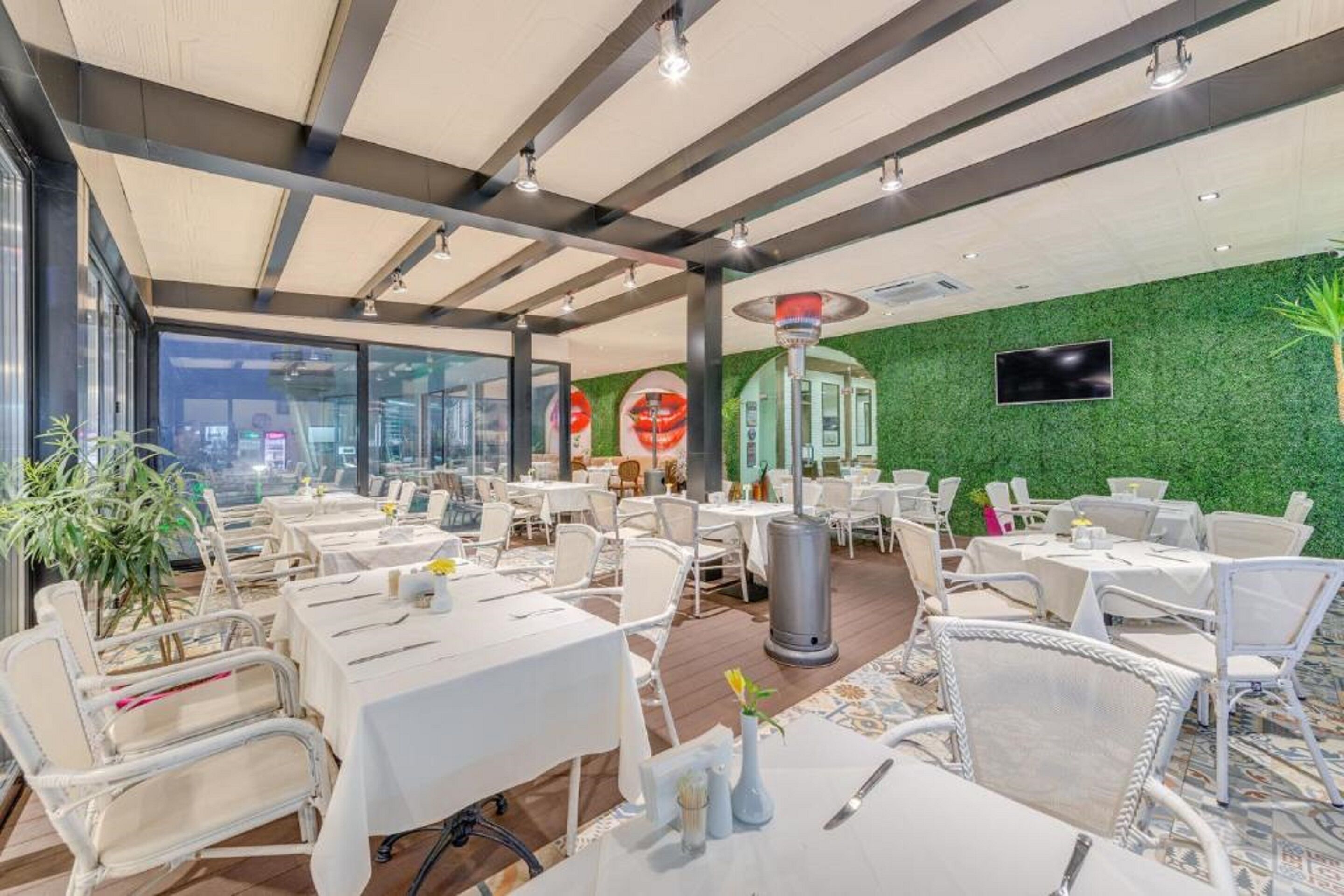 Un restaurante con mesas dentro y fuera, una pared verde y vistas a la ciudad.