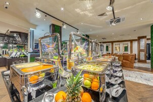 Un área de bufé con varias estaciones de autoservicio, que incluyen frutas y diferentes opciones de comida.
