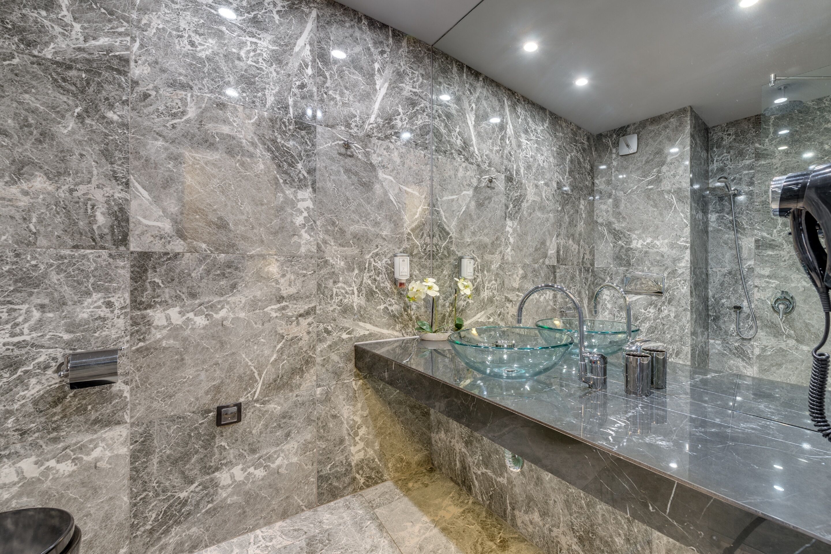 A modern bathroom with marble walls, a glass sink, and a handheld shower.