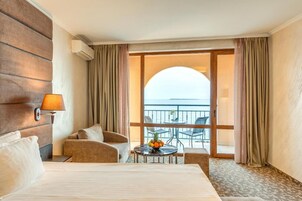 Habitación de hotel con cama, zona de estar con mesa y balcón con vista al mar.