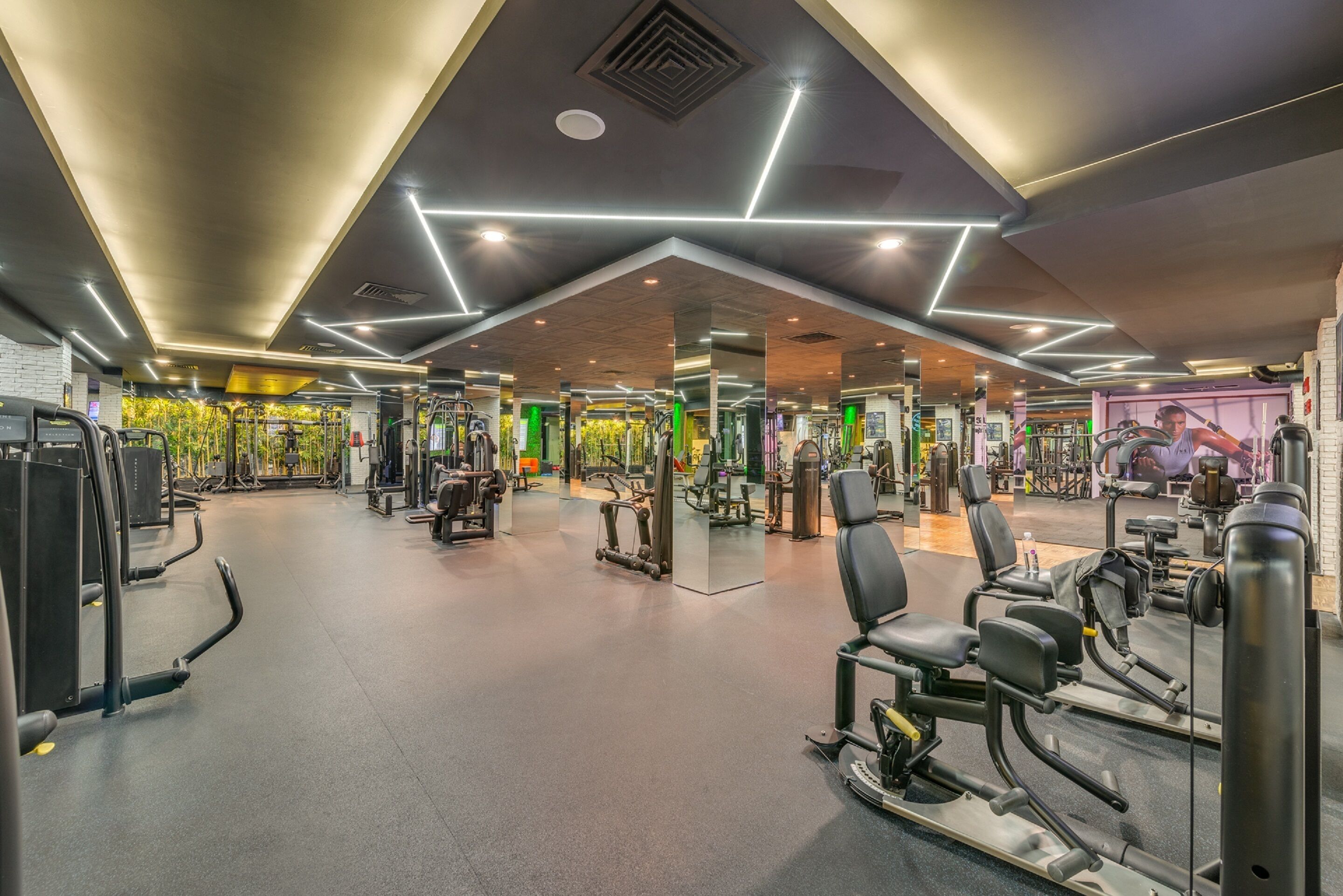 Un gimnasio moderno con diversas máquinas de ejercicio, espejos y un diseño de techo bien iluminado.