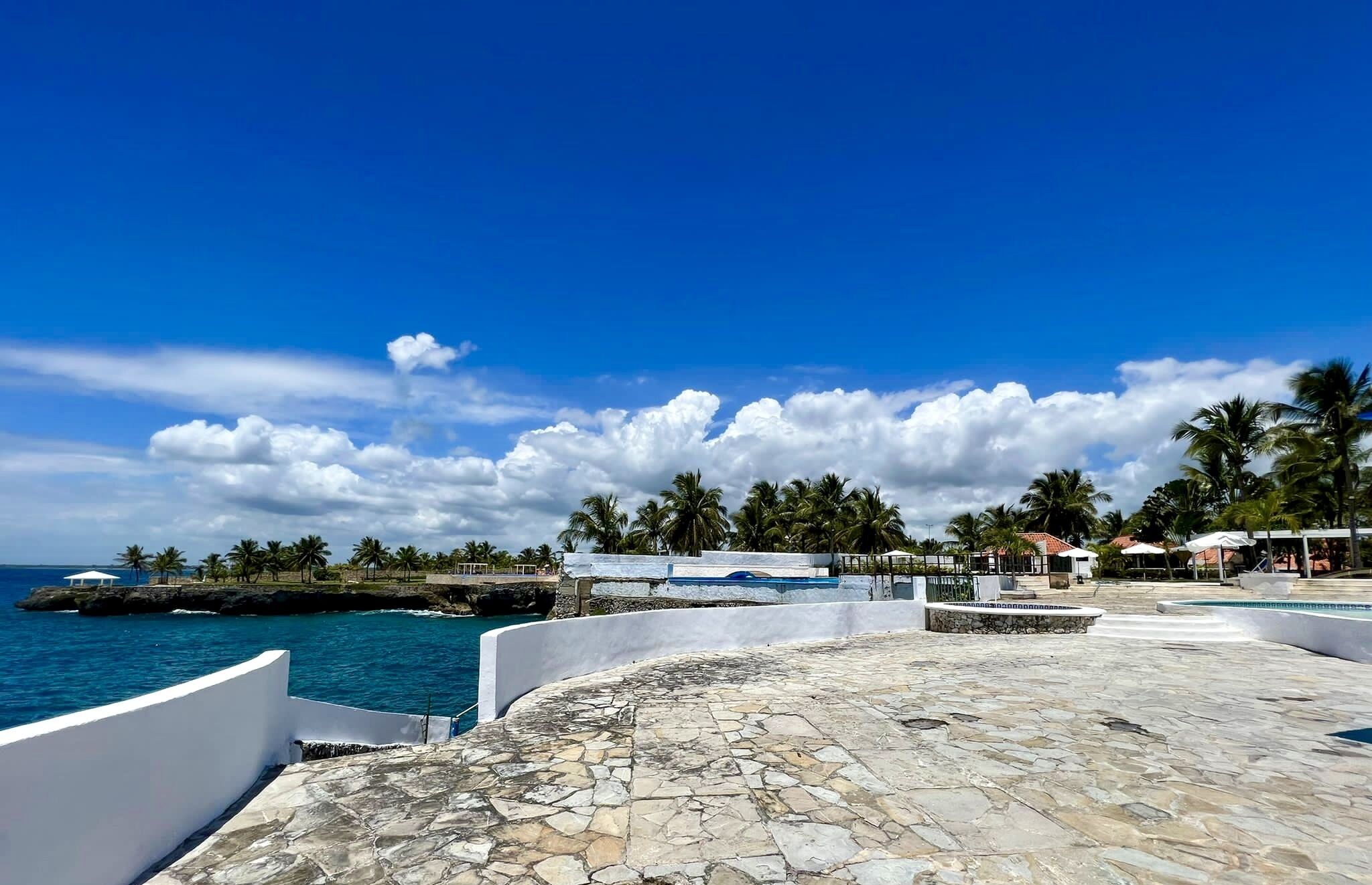 A coastal area with a stone-paved patio, white walls, and a view of the ocean.