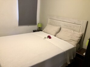 A neatly made bed with a white headboard, a green lamp on a bedside table, and a window with a blind partially drawn. - ON THE Cliff IN THE Caribbean SEA - Villa Maura (Boca Chica)