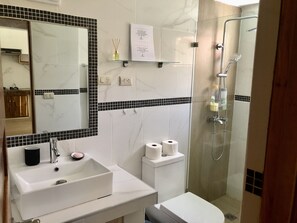 A bathroom with a white sink, mirror, and toilet, a shower with glass doors, and a small shelf with toiletries. - ON THE Cliff IN THE Caribbean SEA - Villa Maura (Boca Chica)