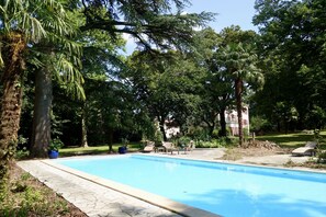 Une piscine entourée d’arbres et un espace patio aménagé avec du mobilier d’extérieur.