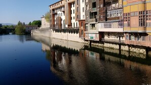 Ein mehrstöckiges Gebäude am Flussufer, mit Balkonen und einer Brücke über dem Wasser.