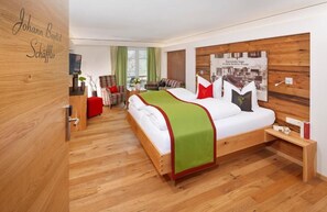 Ein modernes Hotelzimmer mit Holzboden, einem großen Bett mit grüner Decke, einem Holz-Kopfteil und einem kleinen Tisch mit einem roten Stuhl.