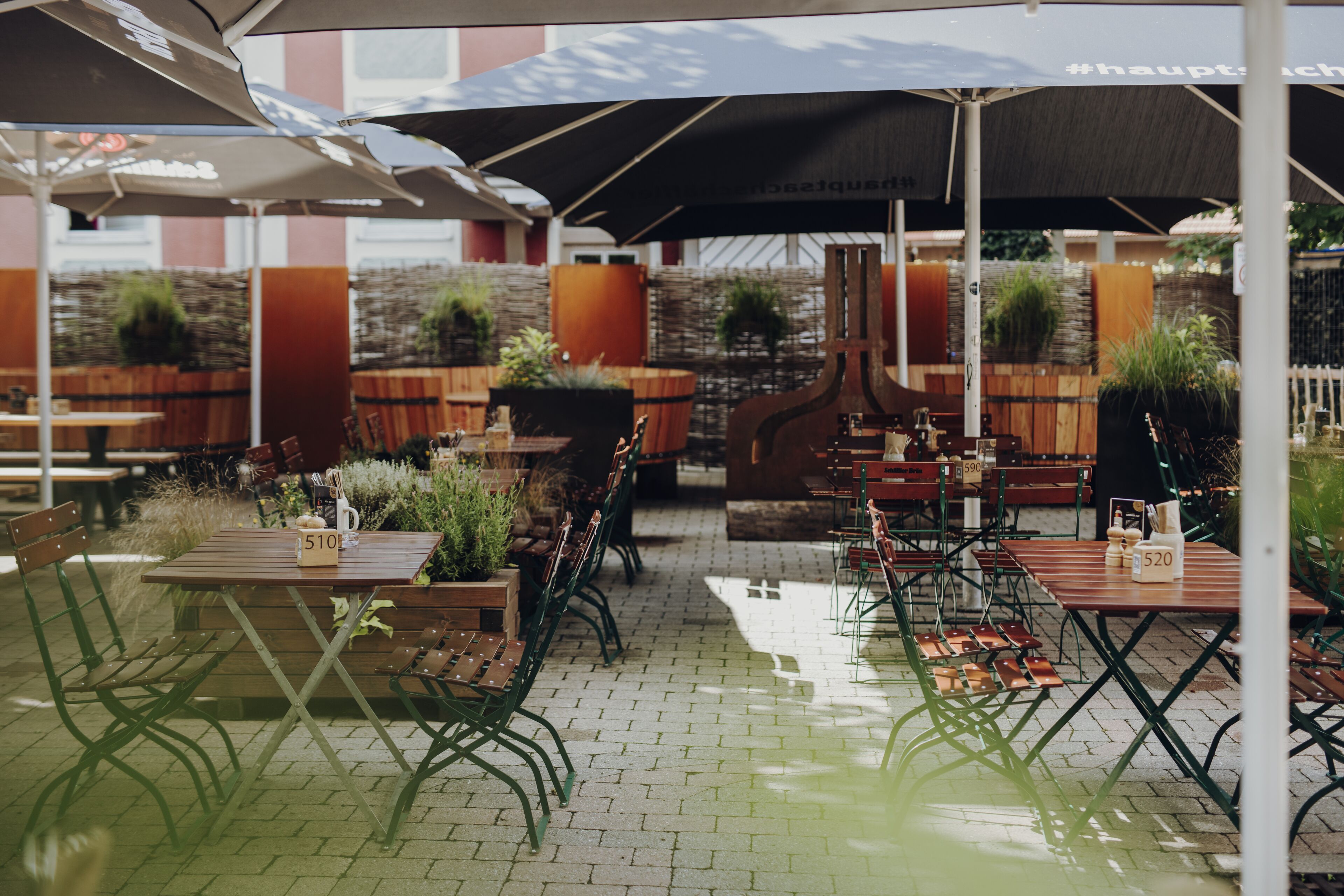 Un café en plein air avec des tables et des chaises en bois, des parasols et des plantes en pot.