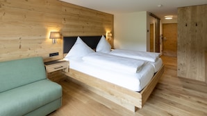 A modern bedroom with a wooden headboard, a bed with white linens, a green sofa, and two bedside lamps. - Brauereigasthof & Hotel Schäffler (Missen-Wilhams)