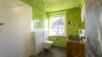 Un baño con cabina de ducha de vidrio, inodoro y lavabo con tocador de madera.