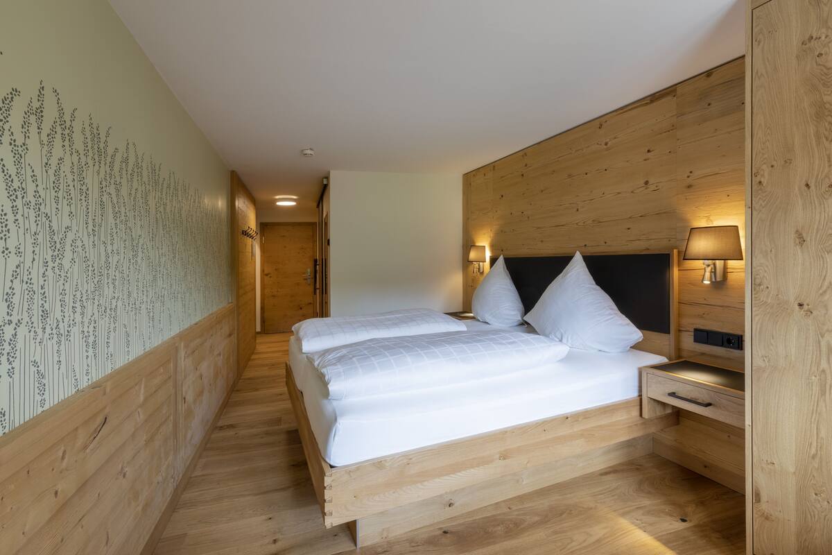 Ein modernes Schlafzimmer mit einem hölzernen Bettgestell, zwei weißen Kissen und einem Nachttisch mit einer Lampe.