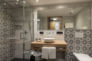 Ein modernes Badezimmer mit einer Glaskabine zur Dusche, einem hölzernen Waschtisch mit großem Becken und gemusterten Fliesen an den Wänden.