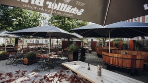 An outdoor seating area with wooden tables and chairs, covered by large umbrellas, and a wooden barrel structure. - Brauereigasthof & Hotel Schäffler (Missen-Wilhams)