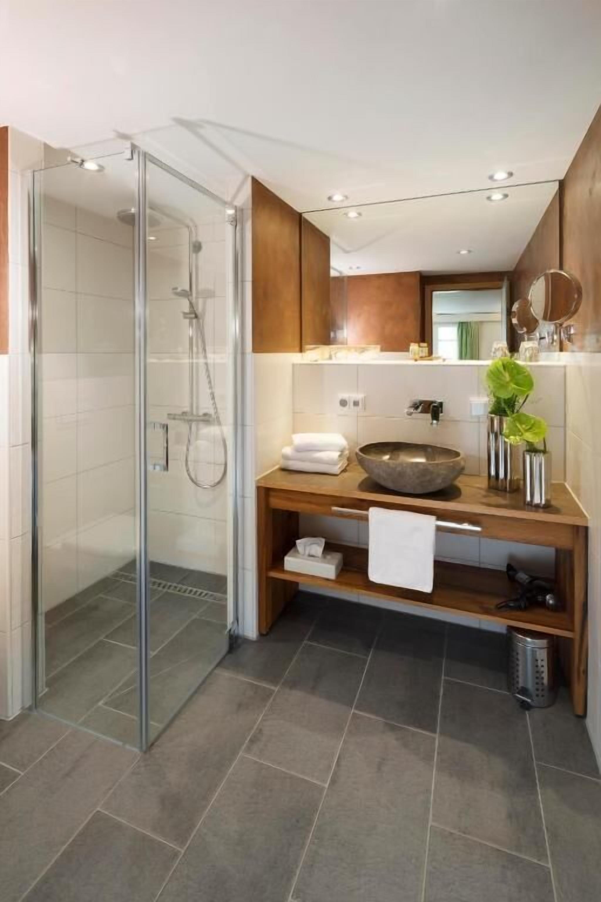 Un bagno moderno con doccia vetrata, un mobile vanitario in legno con lavabo capiente e uno specchio sopra il mobile.