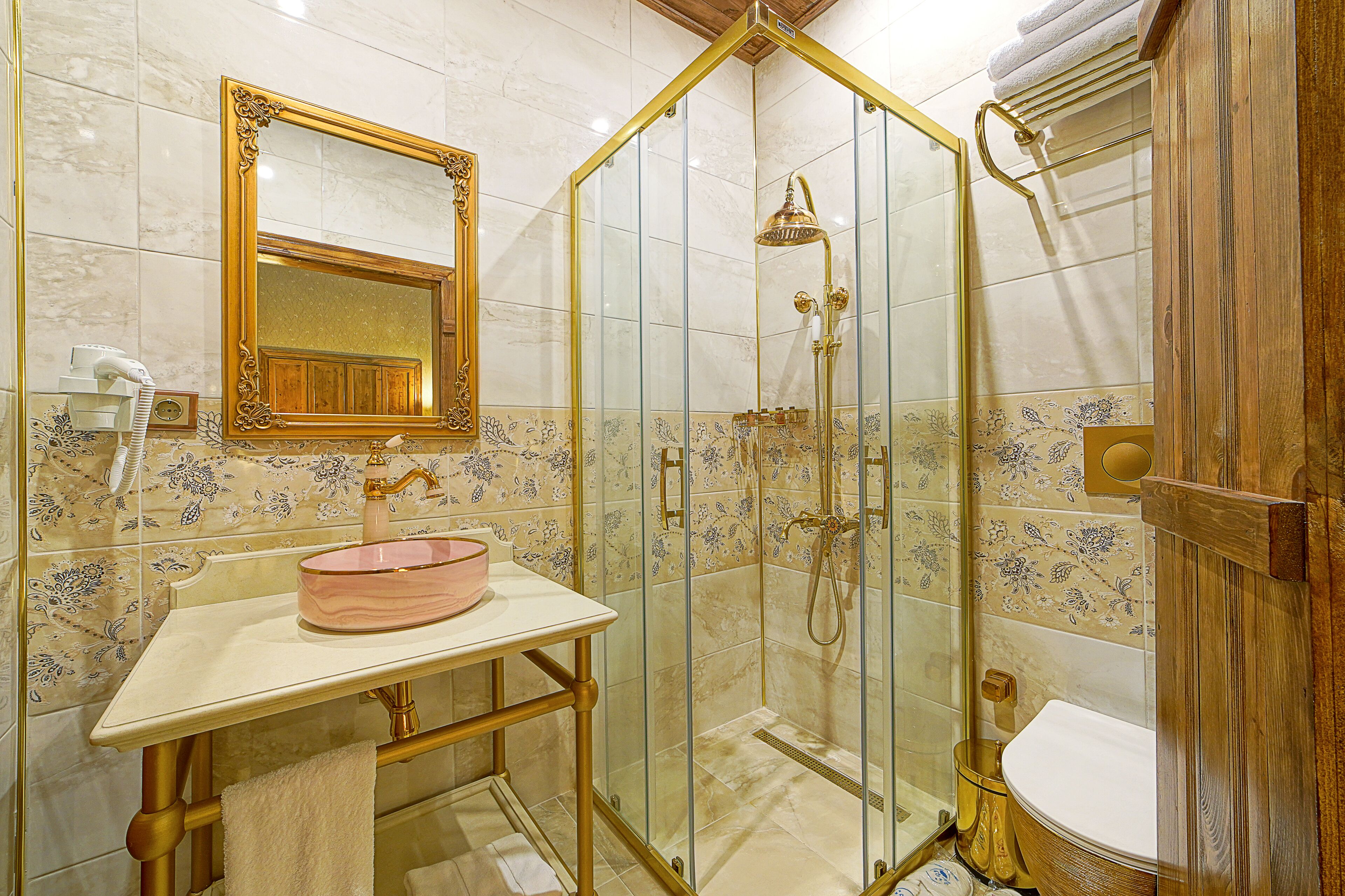 A bathroom with a glass-enclosed shower, a vanity with a pink basin, and a wooden door.