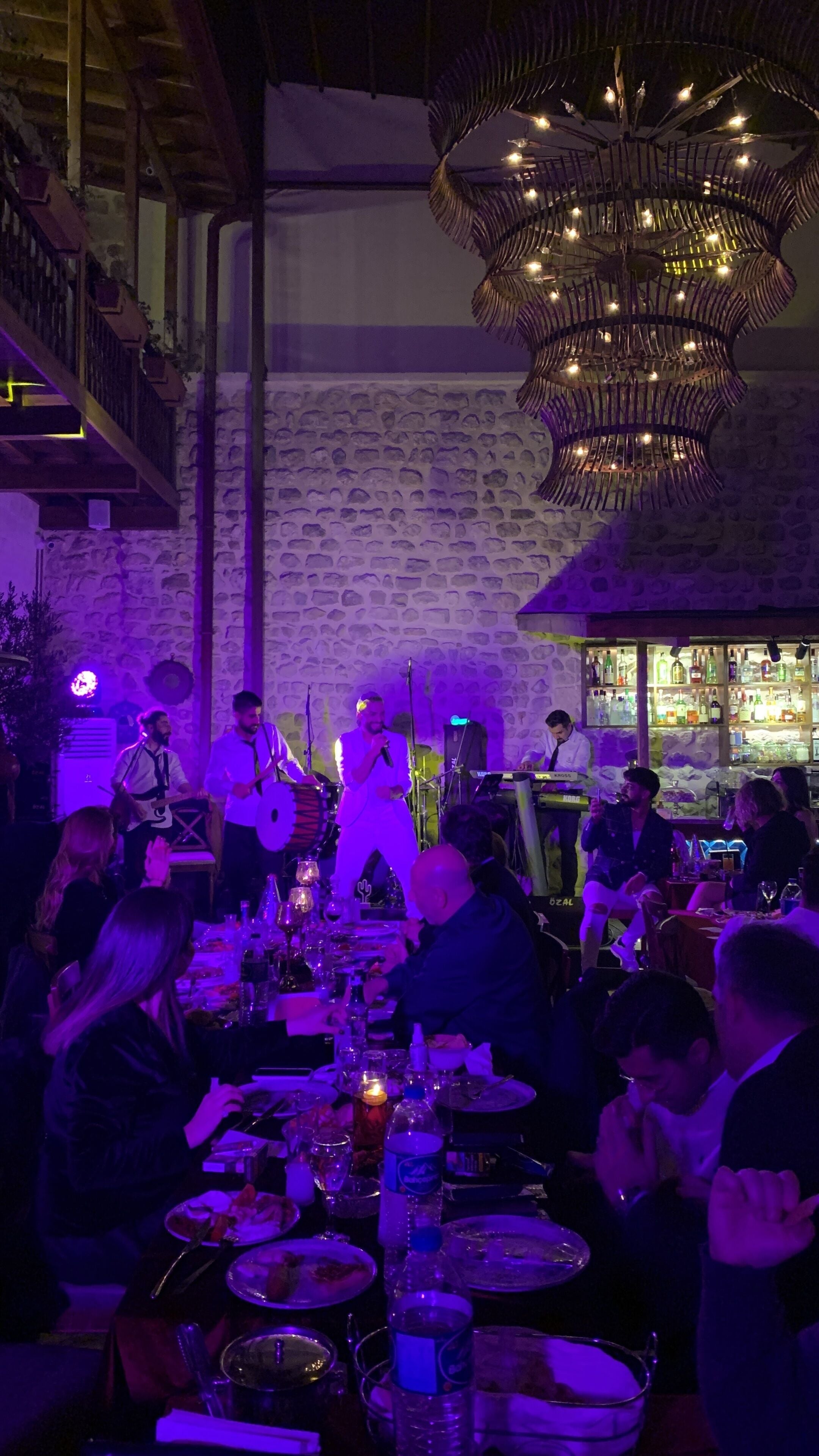 A restaurant with a stone wall backdrop, a chandelier, and a bar area.