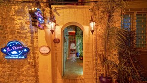 Entrada de un edificio de piedra con un letrero de neón para el restaurante y bar Le Reeve, un arco y plantas en macetas.