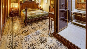 Un dormitorio tradicional con una cama grande, un candelabro ornamentado y un espejo con marco de madera.