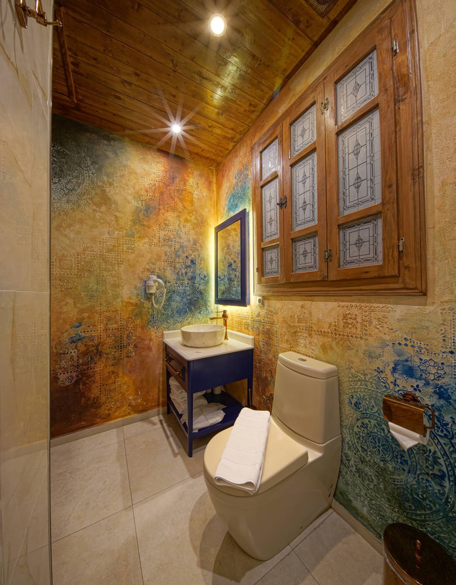 Een badkamer met een houten plafond, een wastafel met spiegel, een toilet en behang met een patroon.