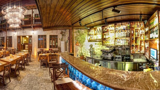 Un restaurante con zona de bar, paredes de piedra, mesas de madera y un candelabro.