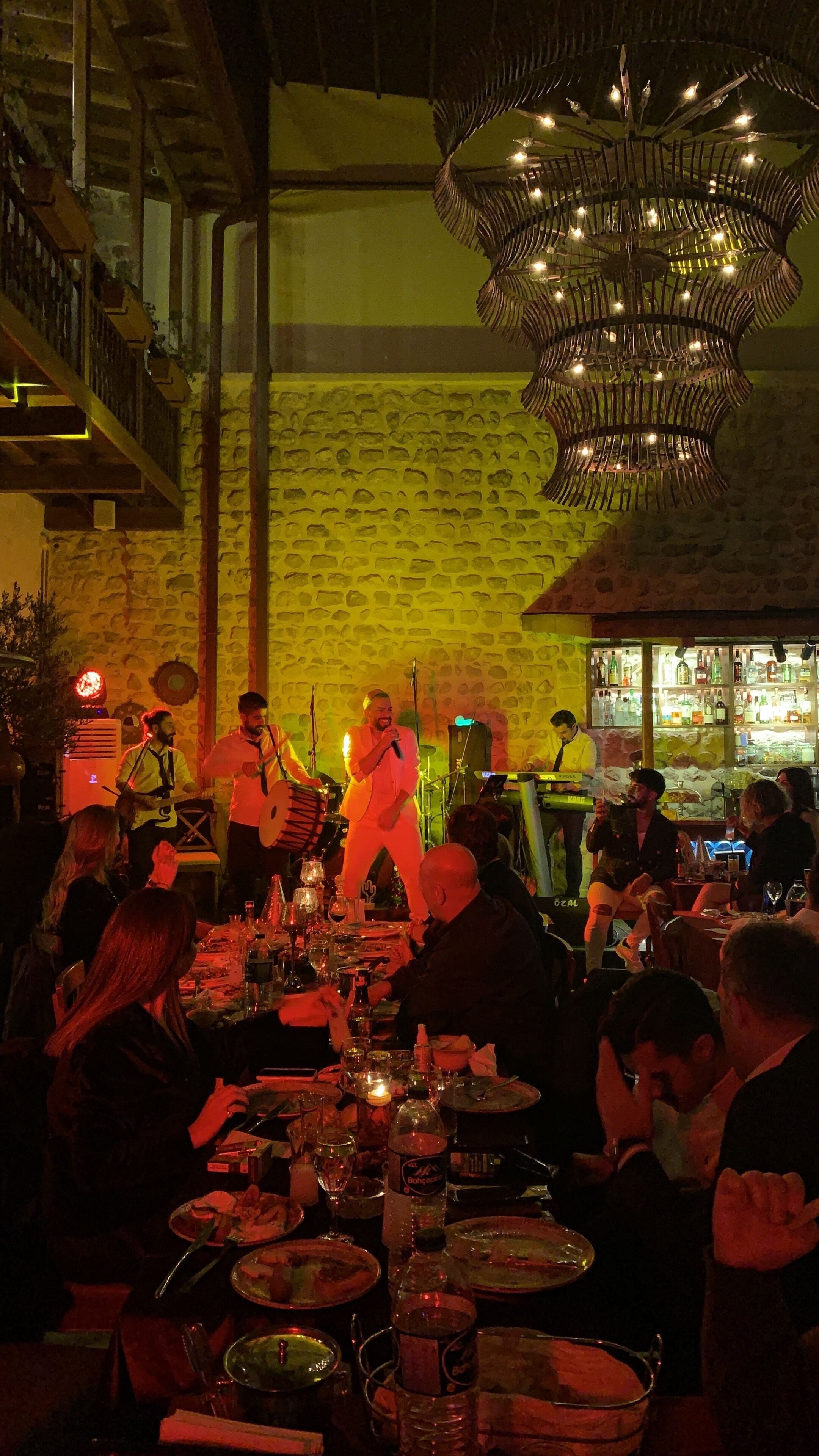 Un restaurante con pared de piedra, una araña y una banda tocando.