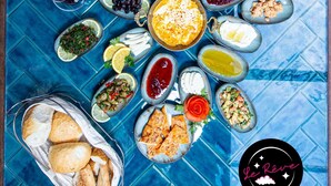 Una mesa con diversos platos y bebidas, como aceitunas, tomates y pan, sobre una superficie de azulejos azules.