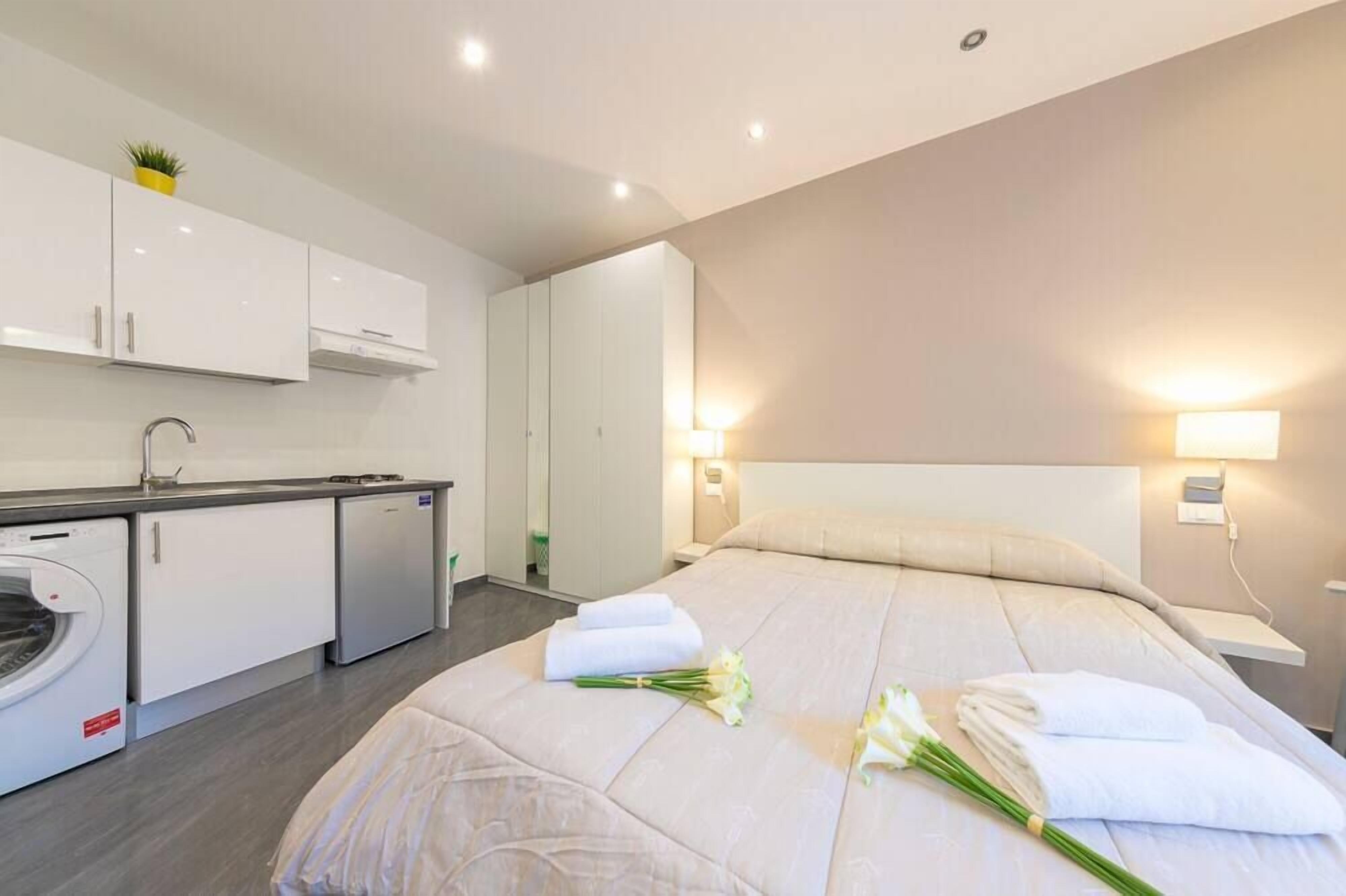 A modern hotel room with a neatly made bed, a small kitchenette, and a bathroom.