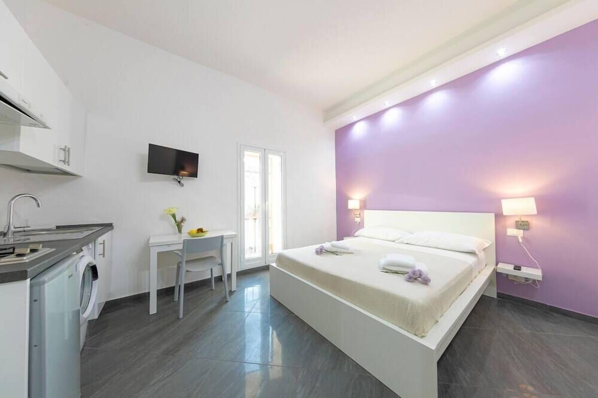 A modern hotel room with a bed, a desk, a washing machine, and a TV.