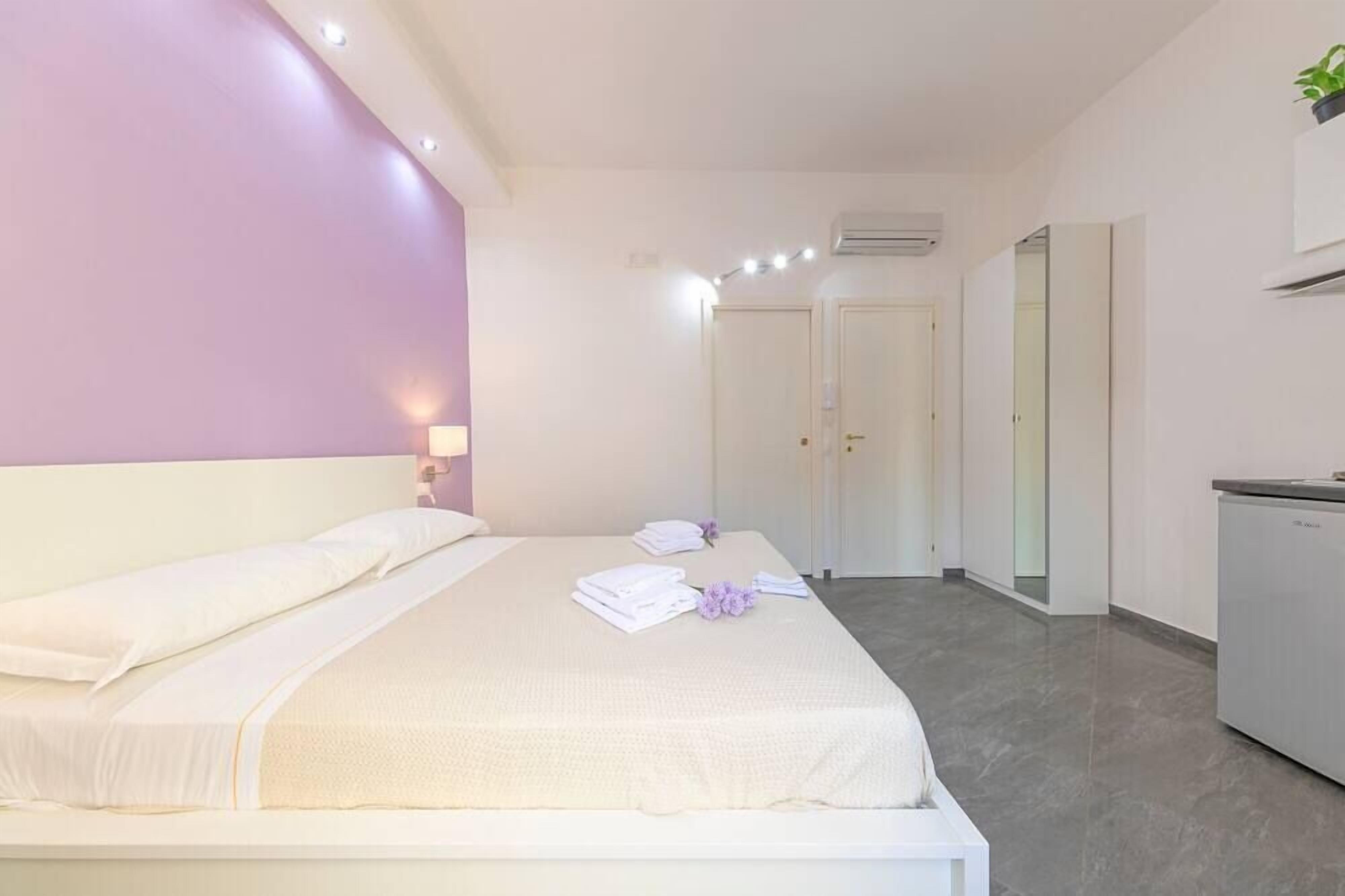 Una habitación de hotel moderna con una cama grande, una mesita de noche, un escritorio pequeño y un espejo.
