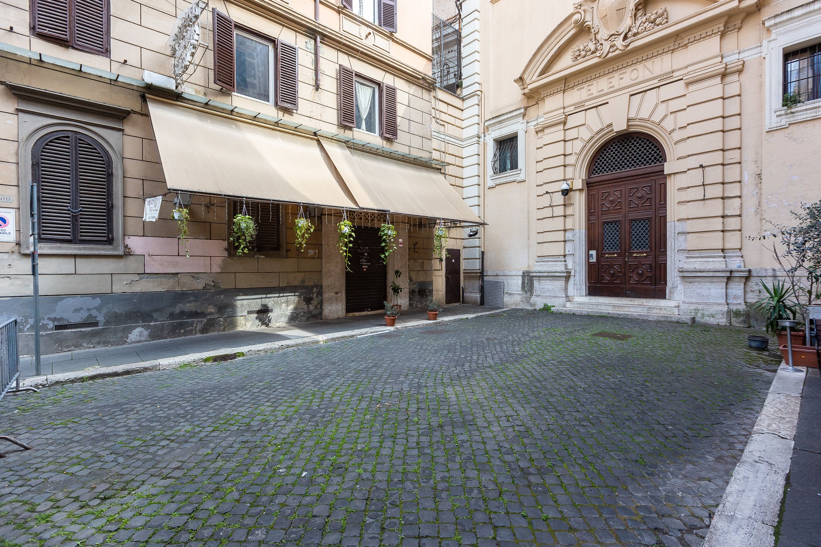 A cobblestone courtyard with a building featuring a large awning and hanging plants.