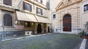 A cobblestone courtyard with a building featuring a large awning and hanging plants. - Lovely New Home, Via Genova (Roma)