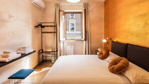 A hotel room with a bed, a bench, a shelf with towels, a radiator, and a window with curtains. - Lovely New Home, Via Genova (Roma)