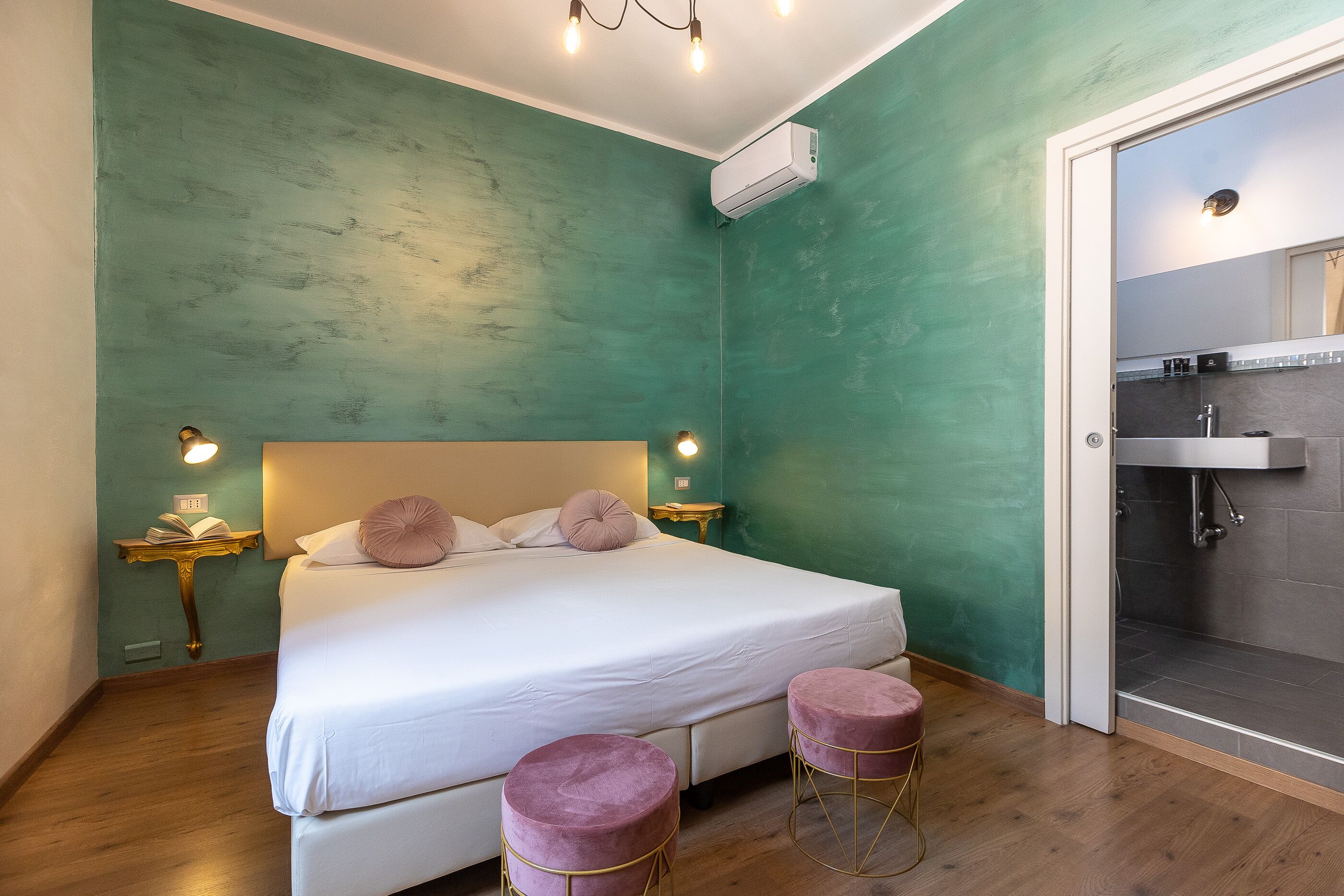 A bedroom with a bed, bedside tables, a nightstand, a reading lamp, and a bathroom with a shower.