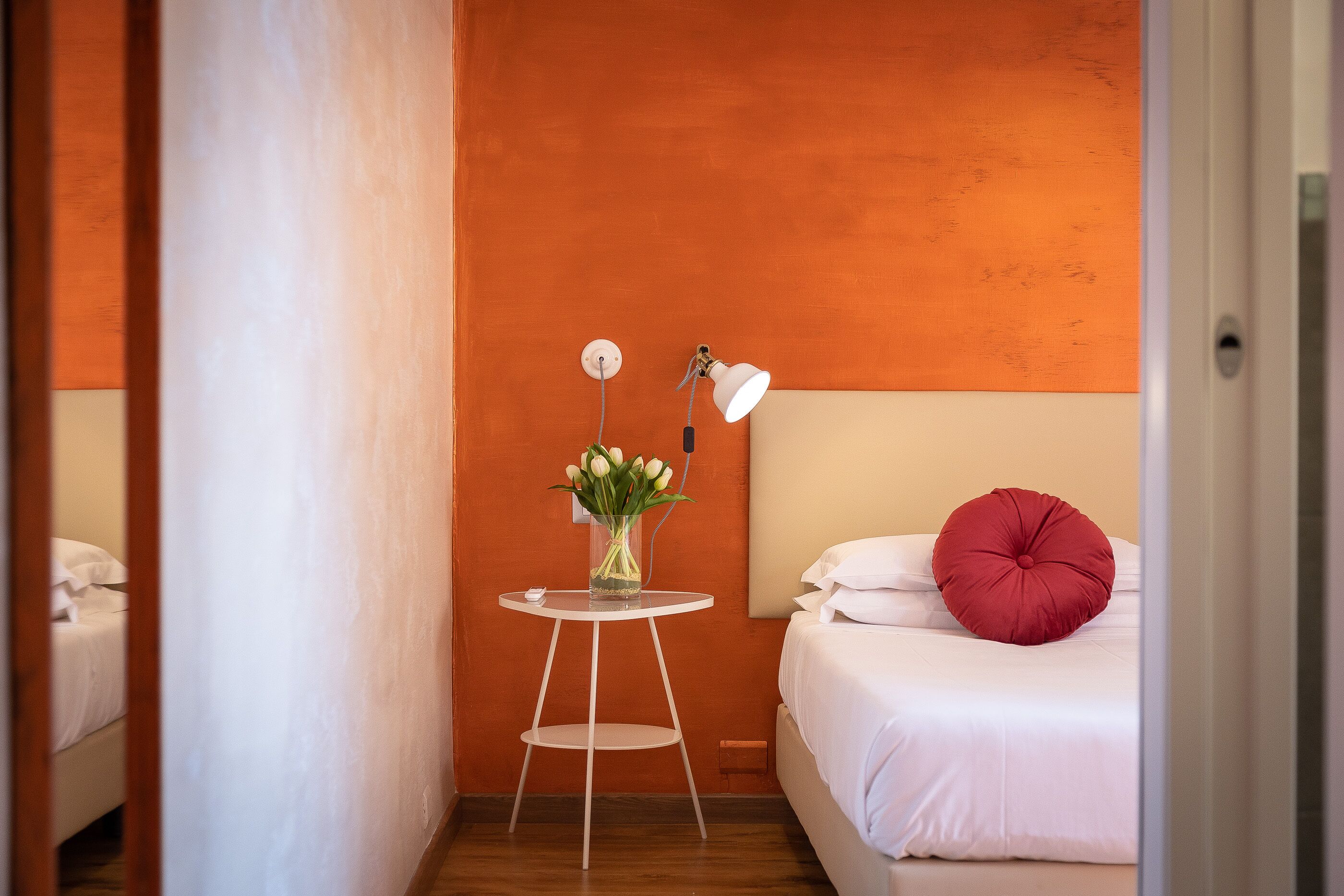 A hotel room with a bed, a small table with a vase of flowers, and a lamp.