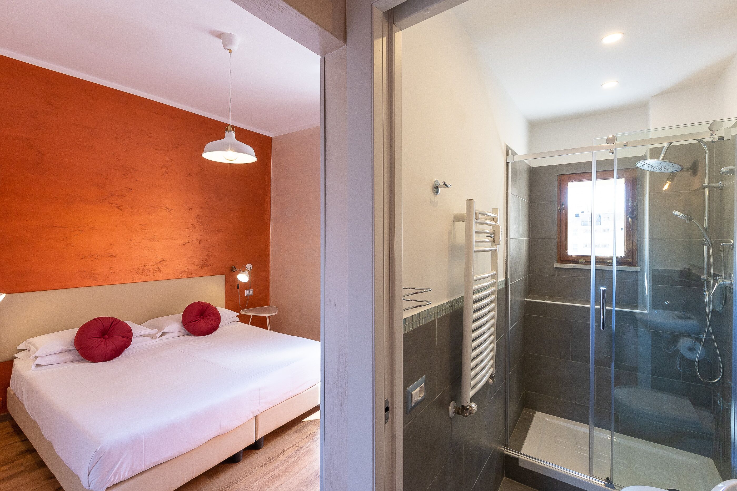 A modern hotel room with a bed, a glass-enclosed shower, and a view of the outside.