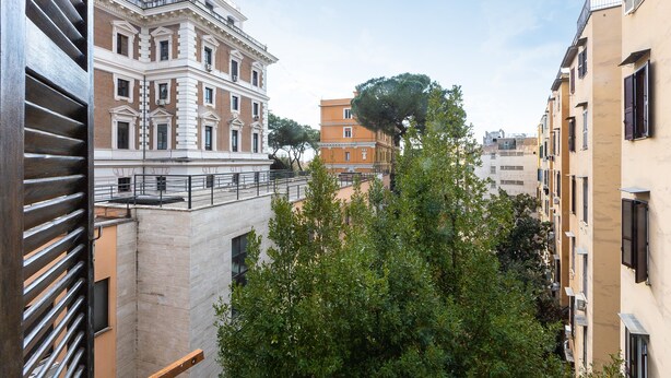 A view of a narrow urban street with buildings, including a prominent classical building with columns and a tree-lined street. - Lovely New Home, Via Genova (Roma)