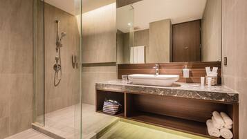 Un baño moderno con ducha envuelta en vidrio, lavamanos de mármol y tocador de madera.